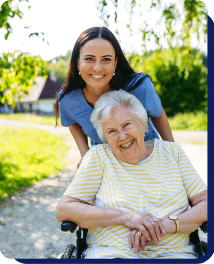 Caregiver smiling with elderly woman in a wheelchair enjoying time outdoors